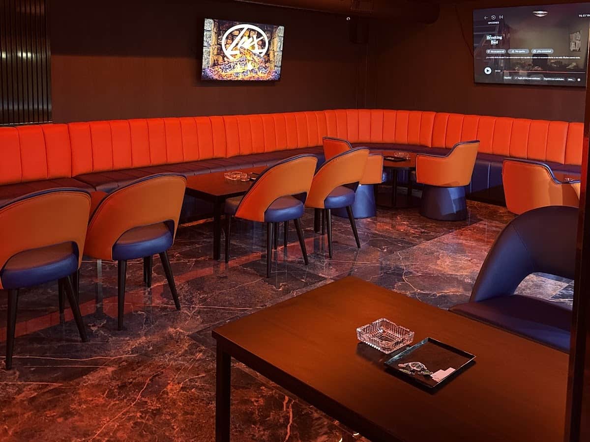 Интерьер клуба Lux Lounge в Марбелье с оранжевыми бархатными диванами, ТВ-экраном и мраморным полом.